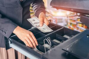 A person is putting money in an open cash register.