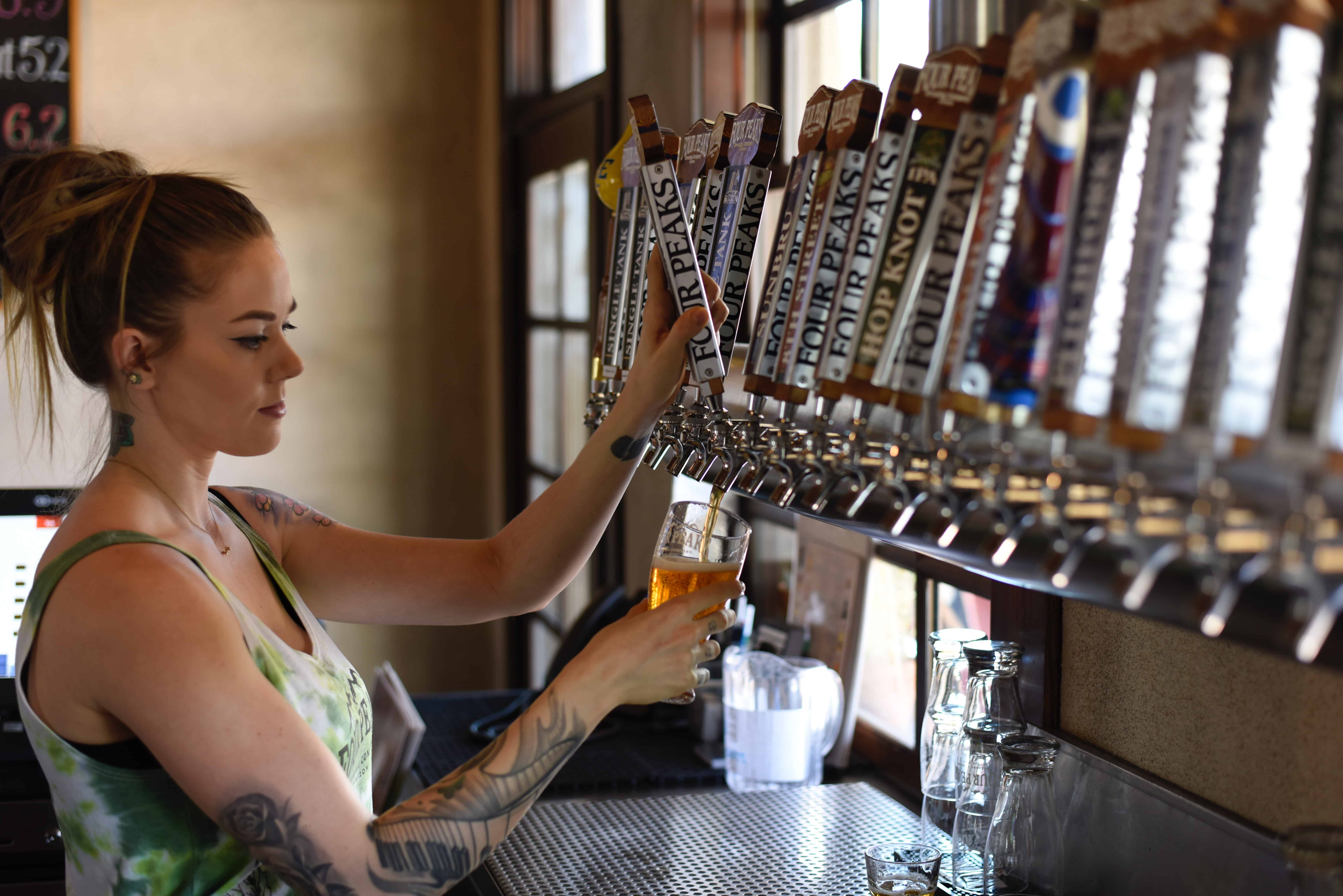 A woman at the bar pouring beer from a tap.