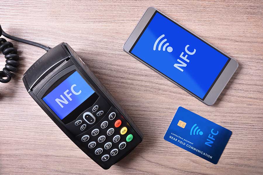 A smart phone and a credit card next to a nfc terminal.