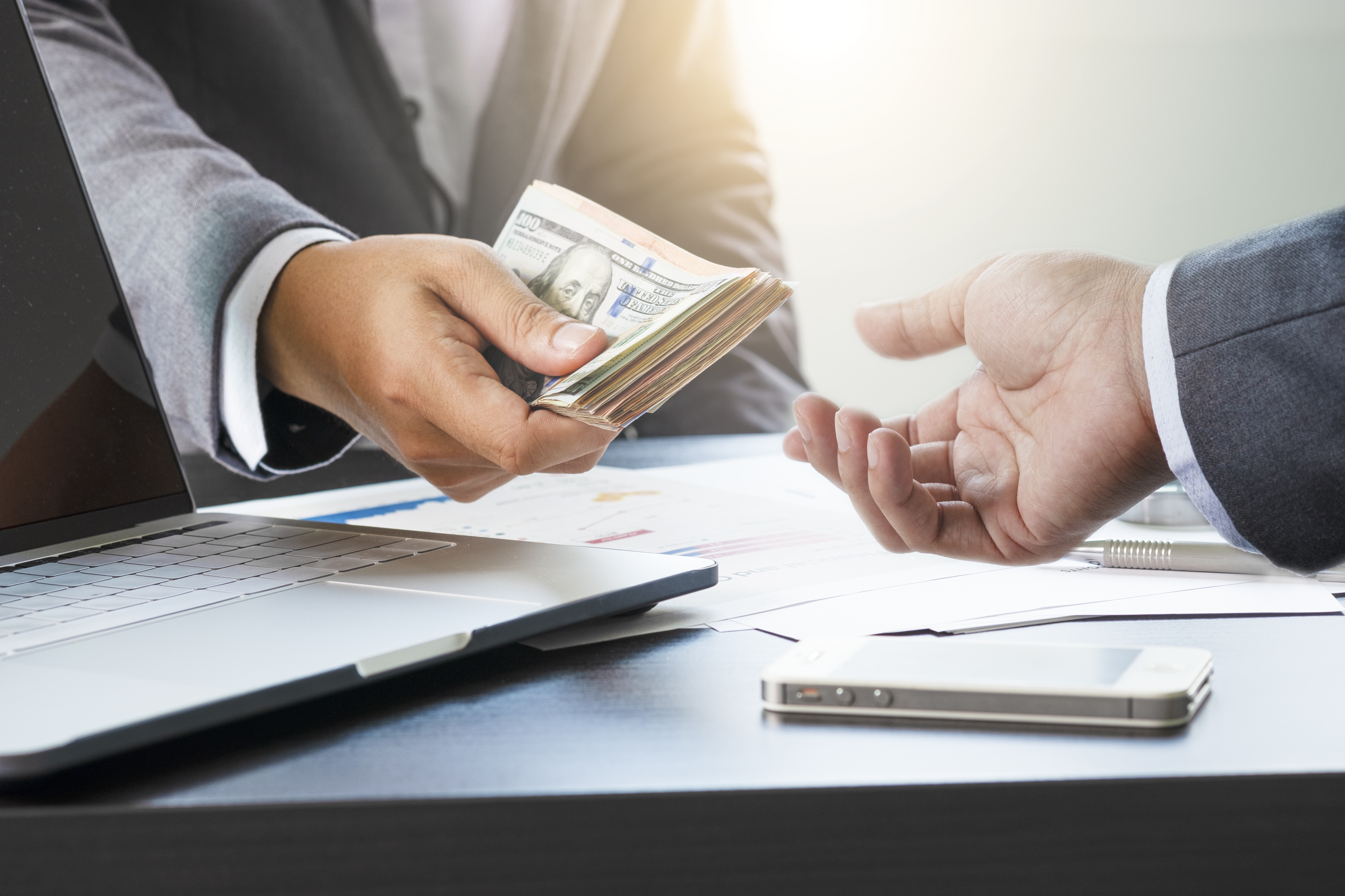 A man in a suit is holding money while another person holds his hand out.