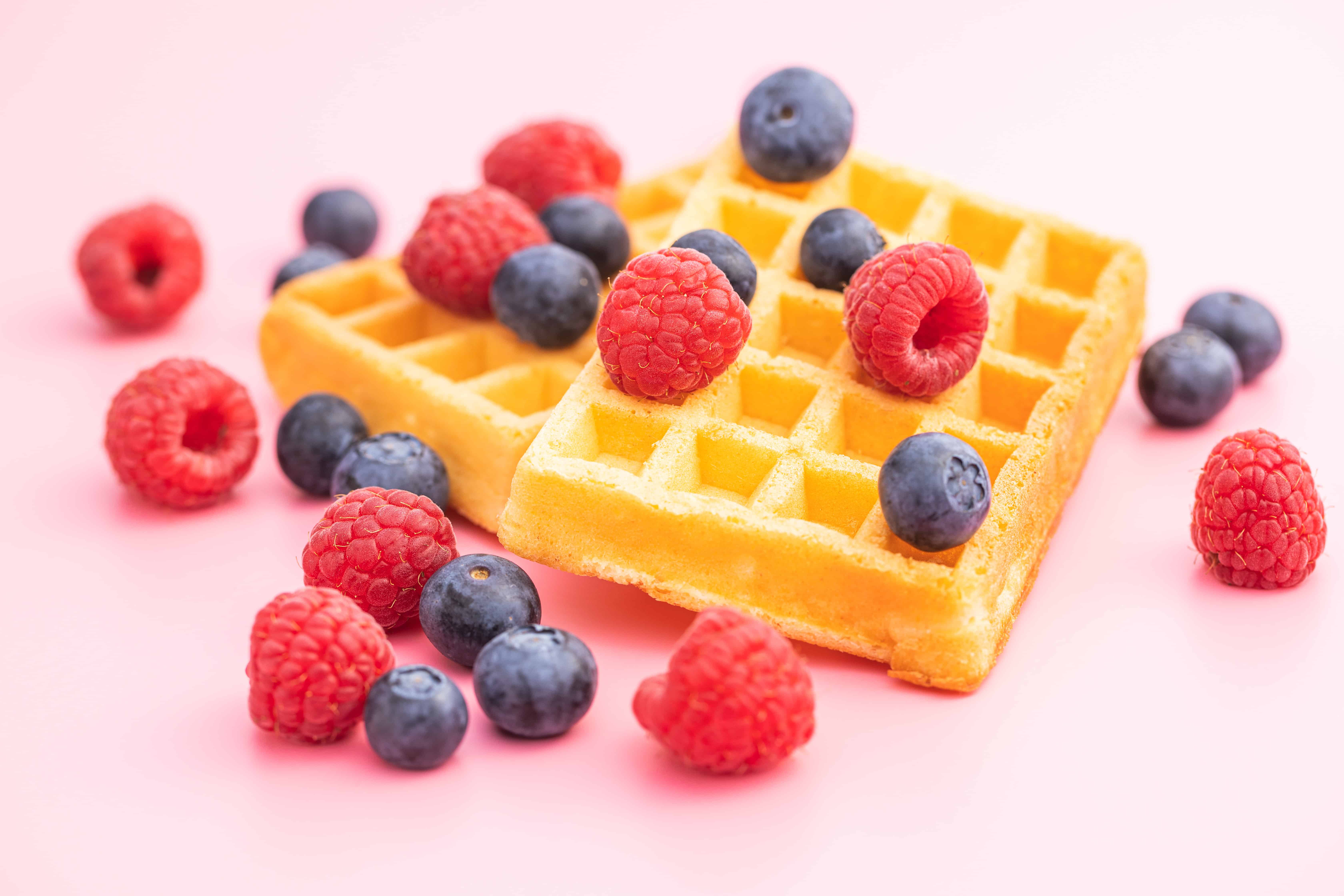 A waffle with raspberries and blueberries on top of it.