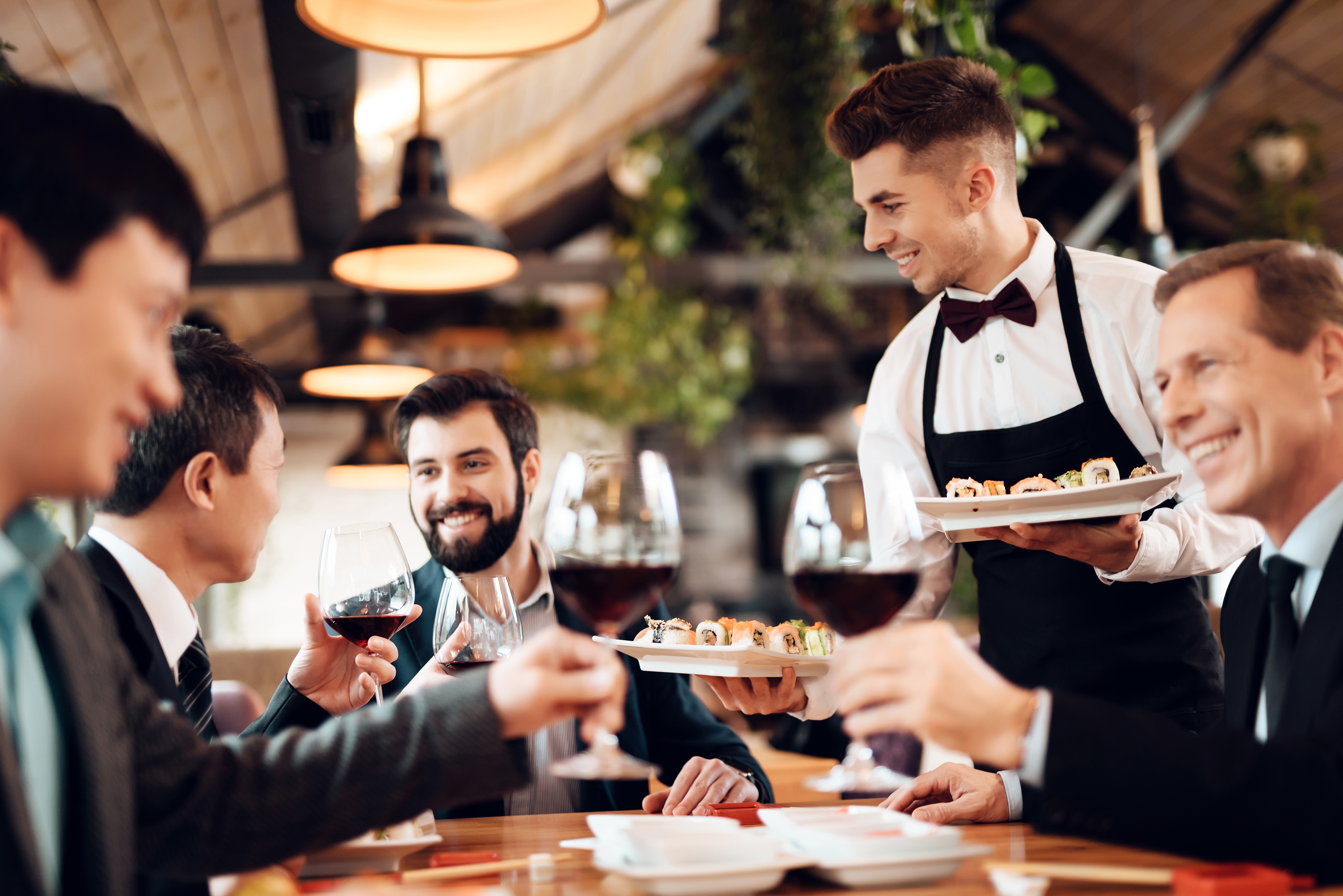 A waiter serving food to two men at a restaurant.