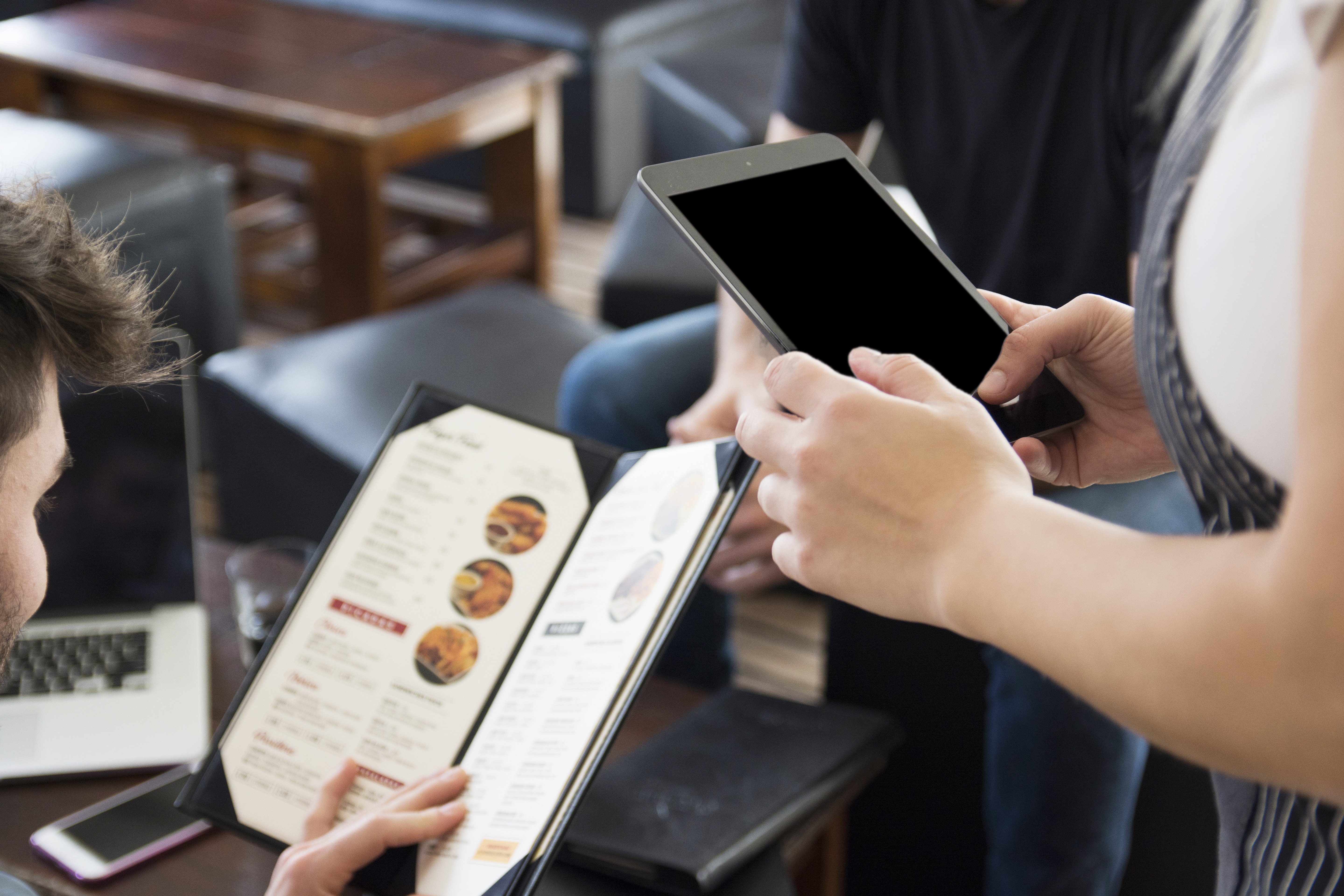 Two people are holding a pizza box and using their tablet.